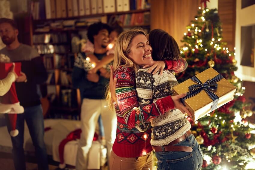 Christmas Eve invitation: woman hugging her friend while holding a gift